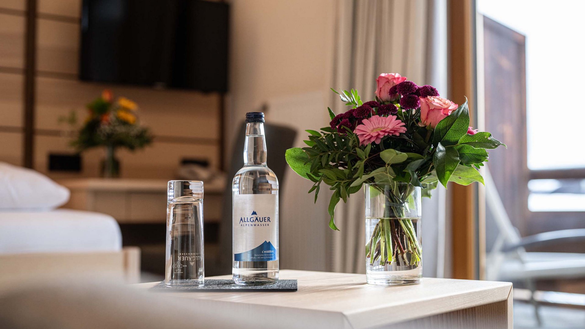 Sustainable hotel in Oberstdorf: for a green holiday in Allgäu Bottle of water, glass, and flower bouquet on wooden table in hotel room