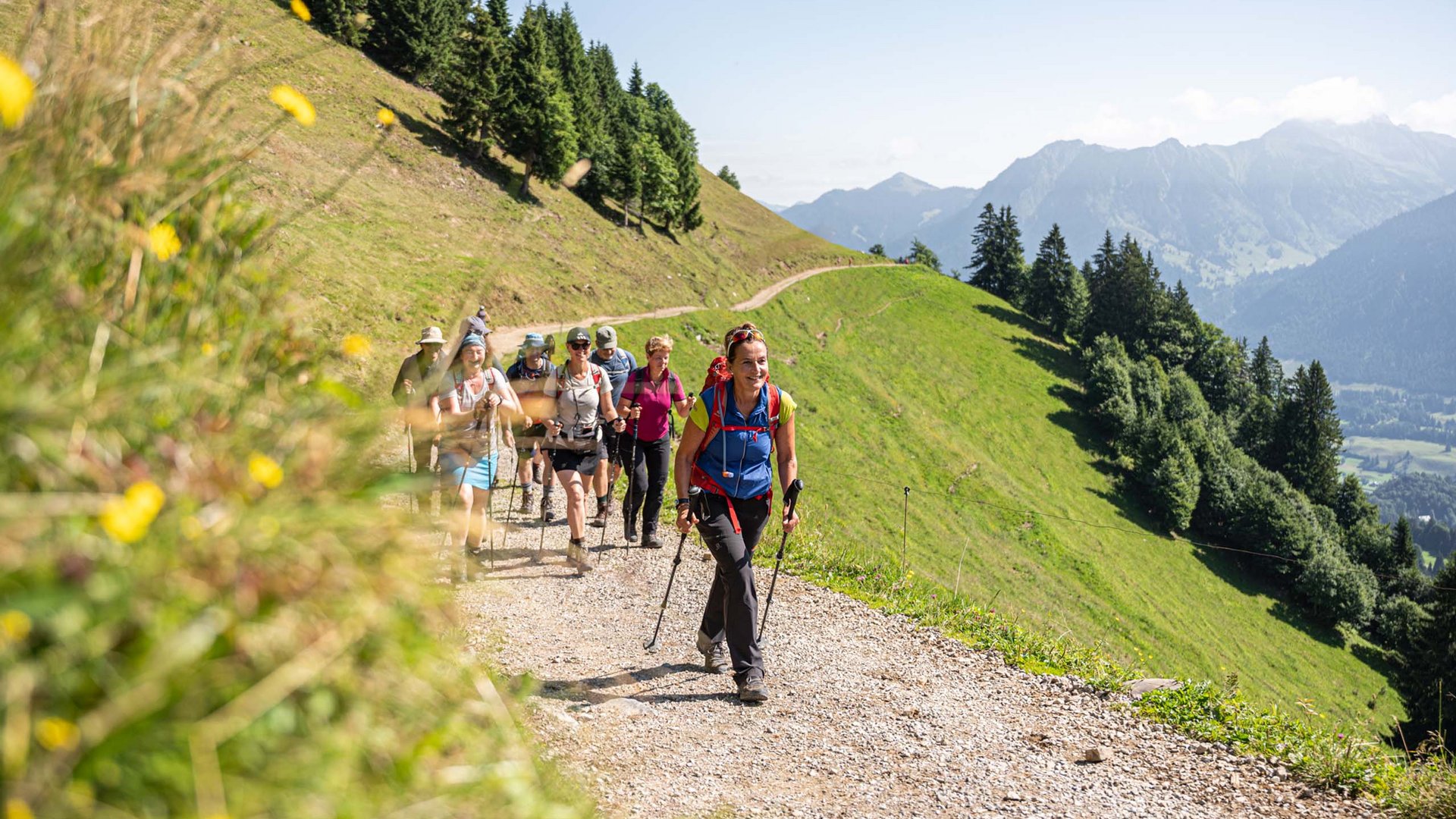 Group hiking on mountain trail with green hills and mountains in background