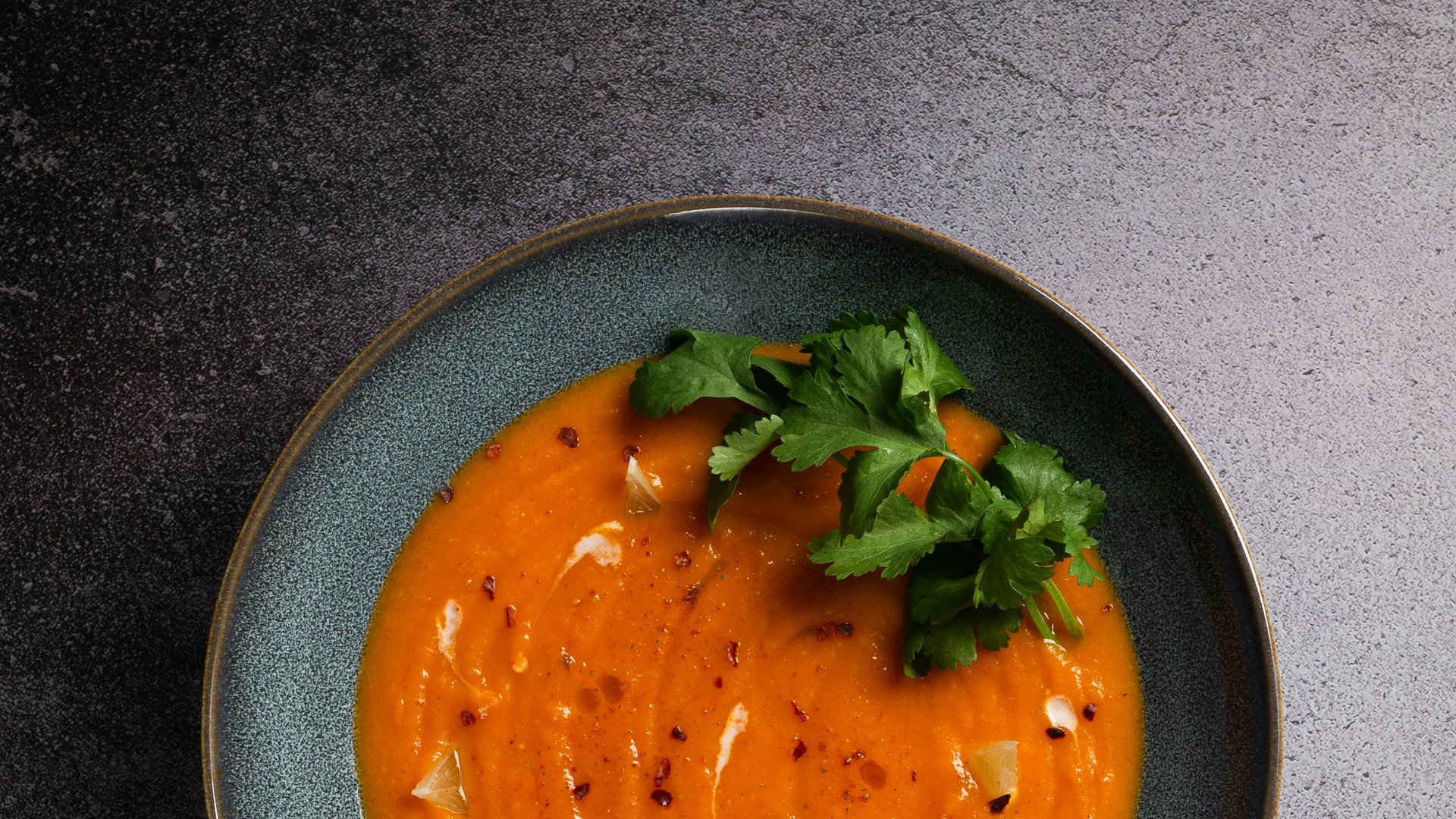 Bowl of creamy carrot soup garnished with cilantro and spices