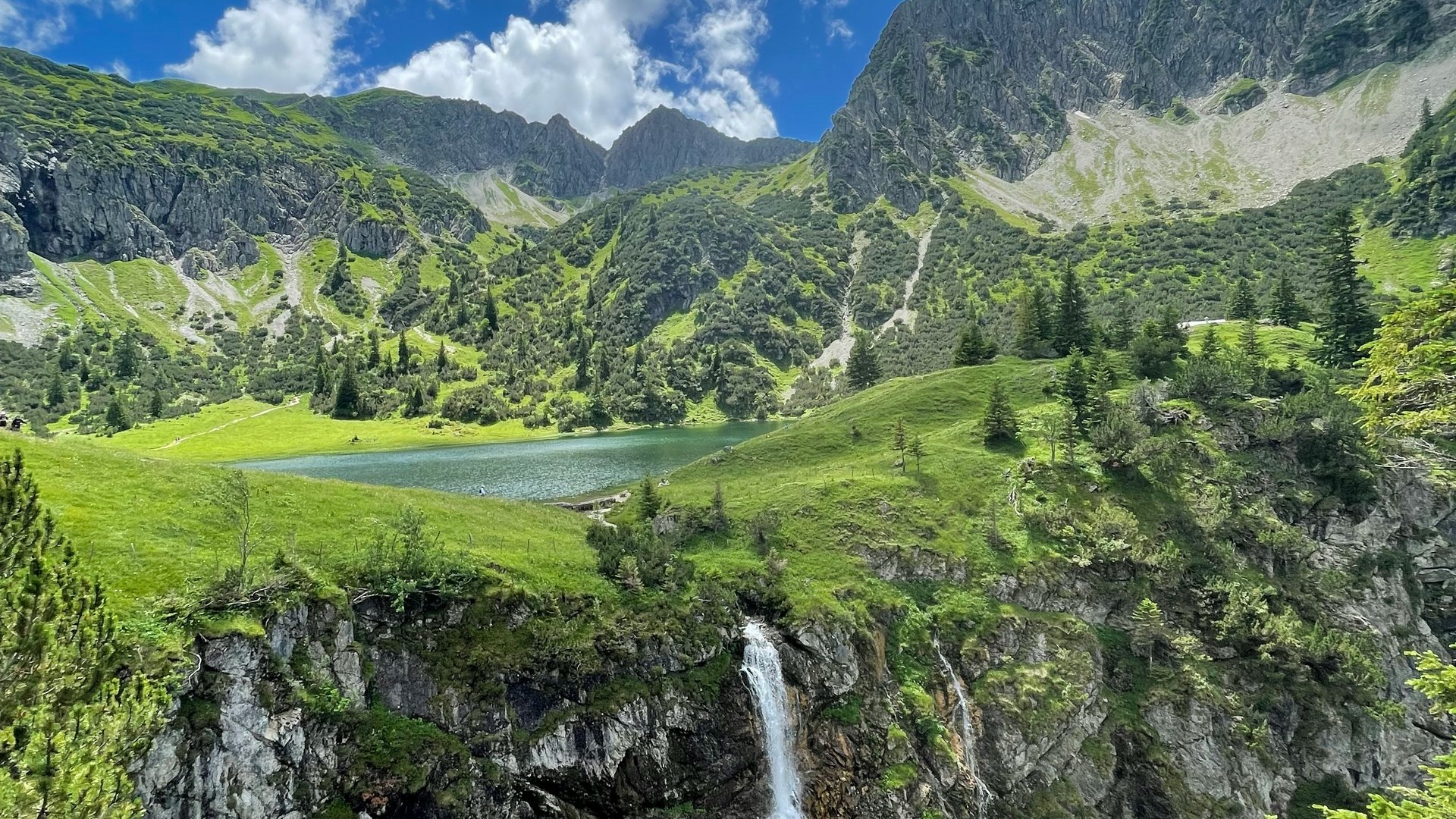 Mountain landscape with waterfall and small lake under blue sky