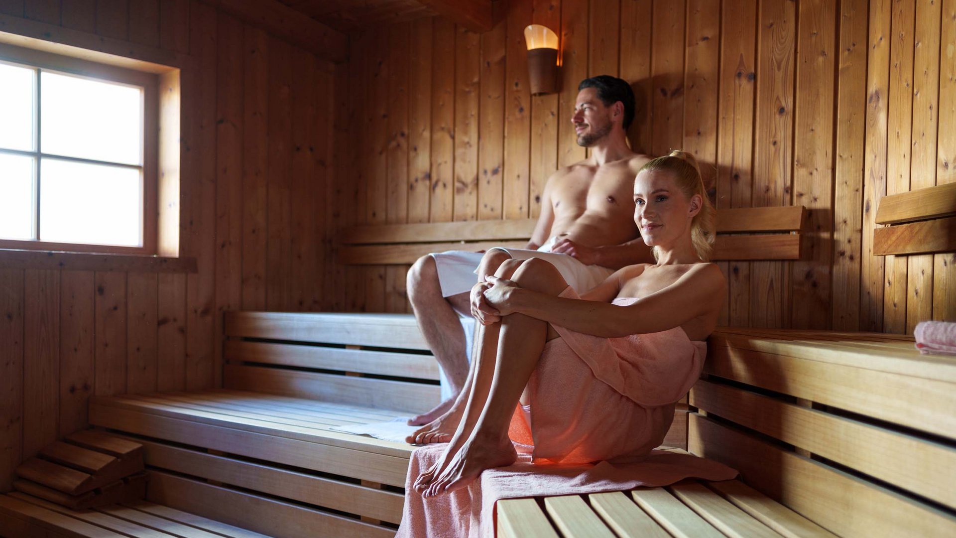Man and woman relaxing in a wooden sauna wrapped in towels