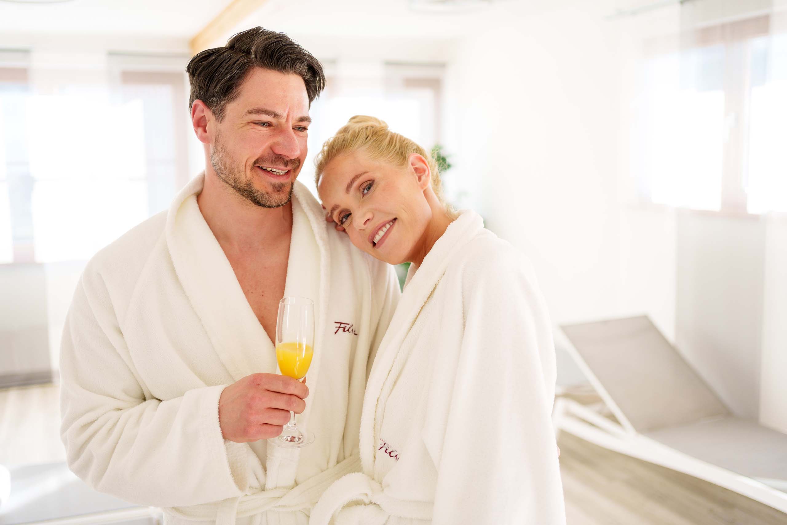 Couple in white bathrobes relaxing with drink at spa